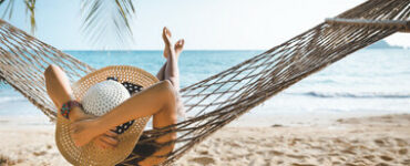 אישה שוכבת על ערסל על חוף הים ומנצלת את ימי החופשה שלה