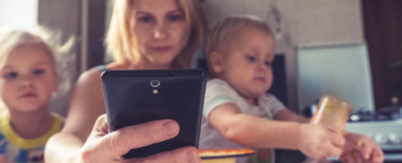 woman holding 2 kids and on phone to show multitasking
