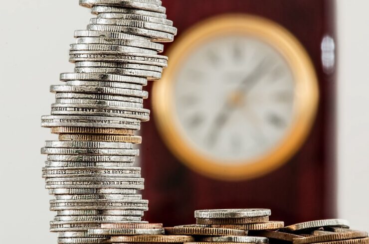 pile of coins on top of a table with clock at the background cost reduction